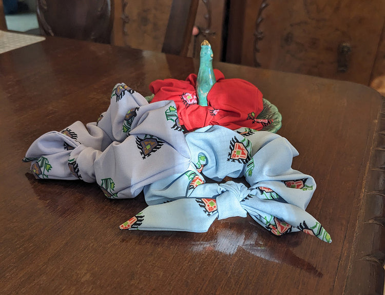 Three beautiful scrunchies, all with vibrant flower patterns. One is red with pink flowers, one is purple with purple flowers, and one is light blue with peach flowers.