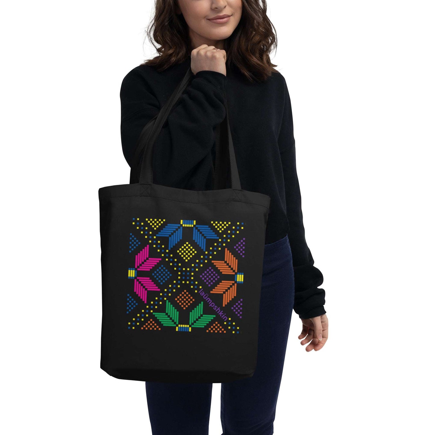 A woman holding a 100% organic cotton black eco reusable shopping tote bag with a colorful pixelated design of flowers and dots.