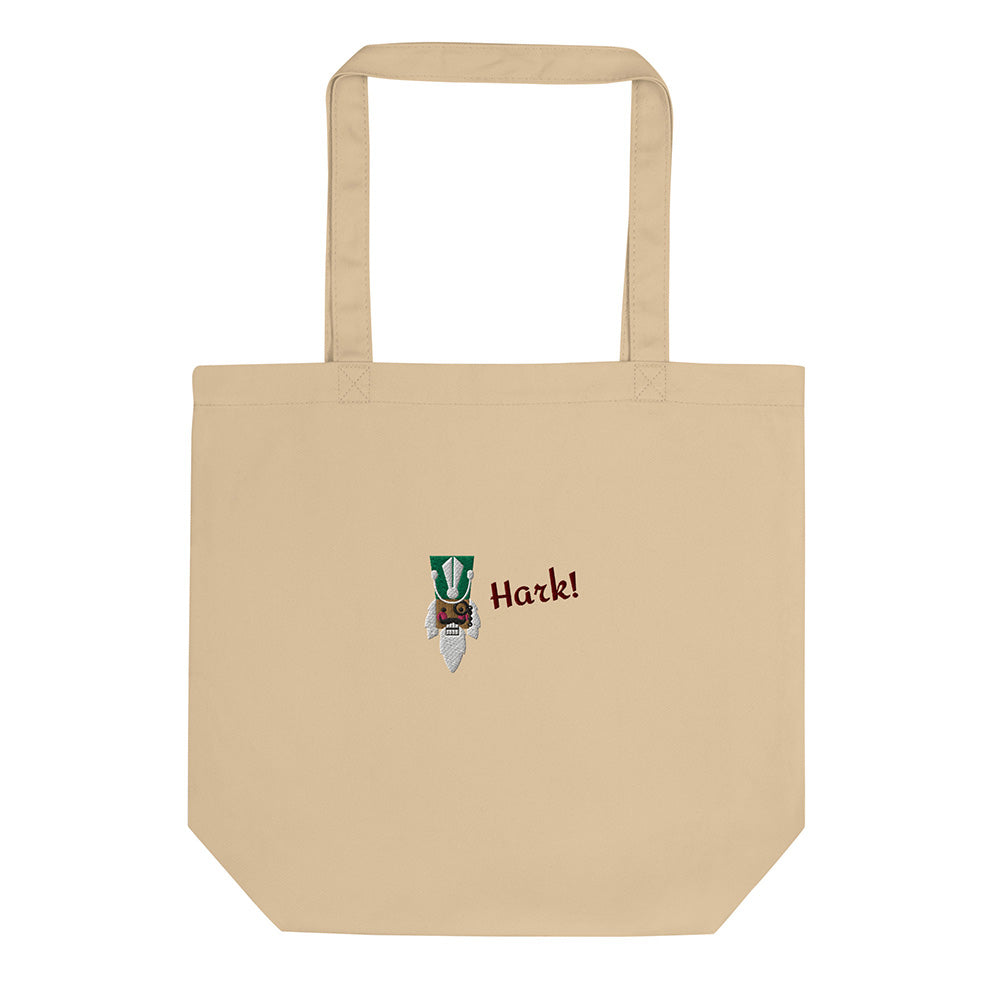 A beige festive holiday tote bag with a large embroidered design on the front. There is the head of a nutcracker wearing a green hat and a monocle and the word "Hark!". It is made of 100% organic cotton.