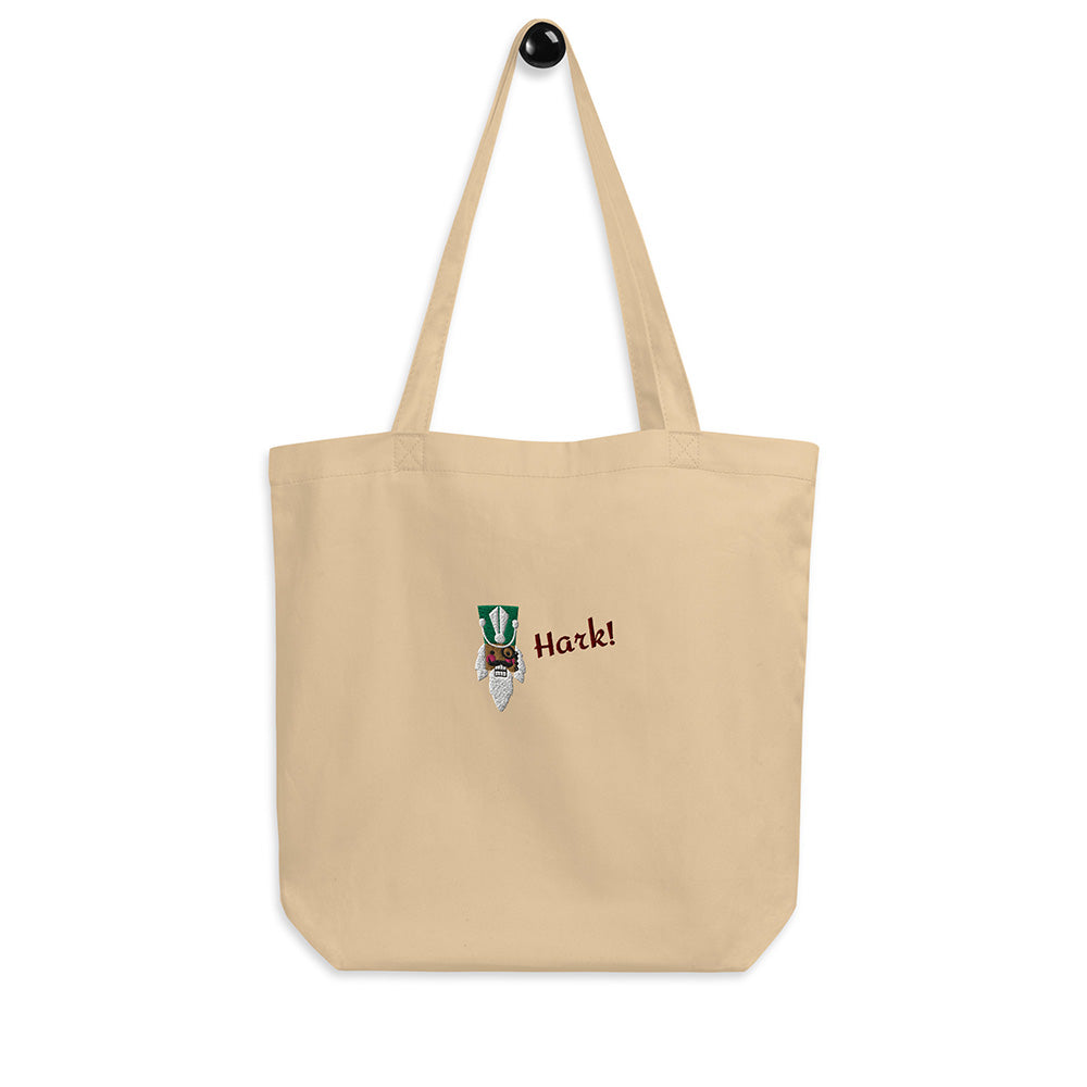 A beige festive holiday tote bag with a large embroidered design on the front. There is the head of a nutcracker wearing a green hat and a monocle and the word "Hark!". It is made of 100% organic cotton.