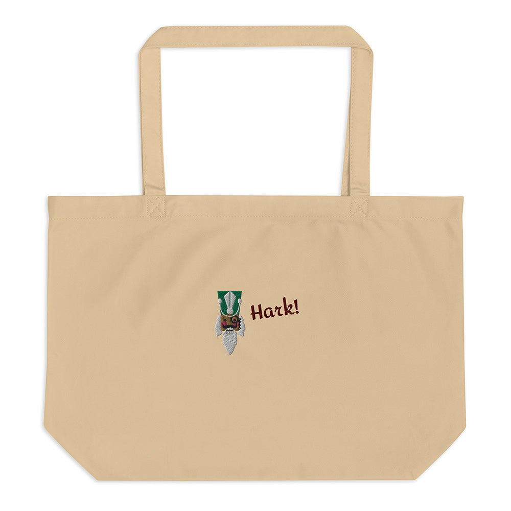 A large beige festive holiday tote bag with a large embroidered design on the front. There is the head of a nutcracker wearing a green hat and a monocle and the word "Hark!". It is made of 100% organic cotton.