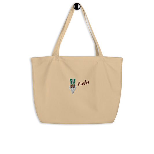 A large beige festive holiday tote bag with a large embroidered design on the front. There is the head of a nutcracker wearing a green hat and a monocle and the word "Hark!". It is made of 100% organic cotton.