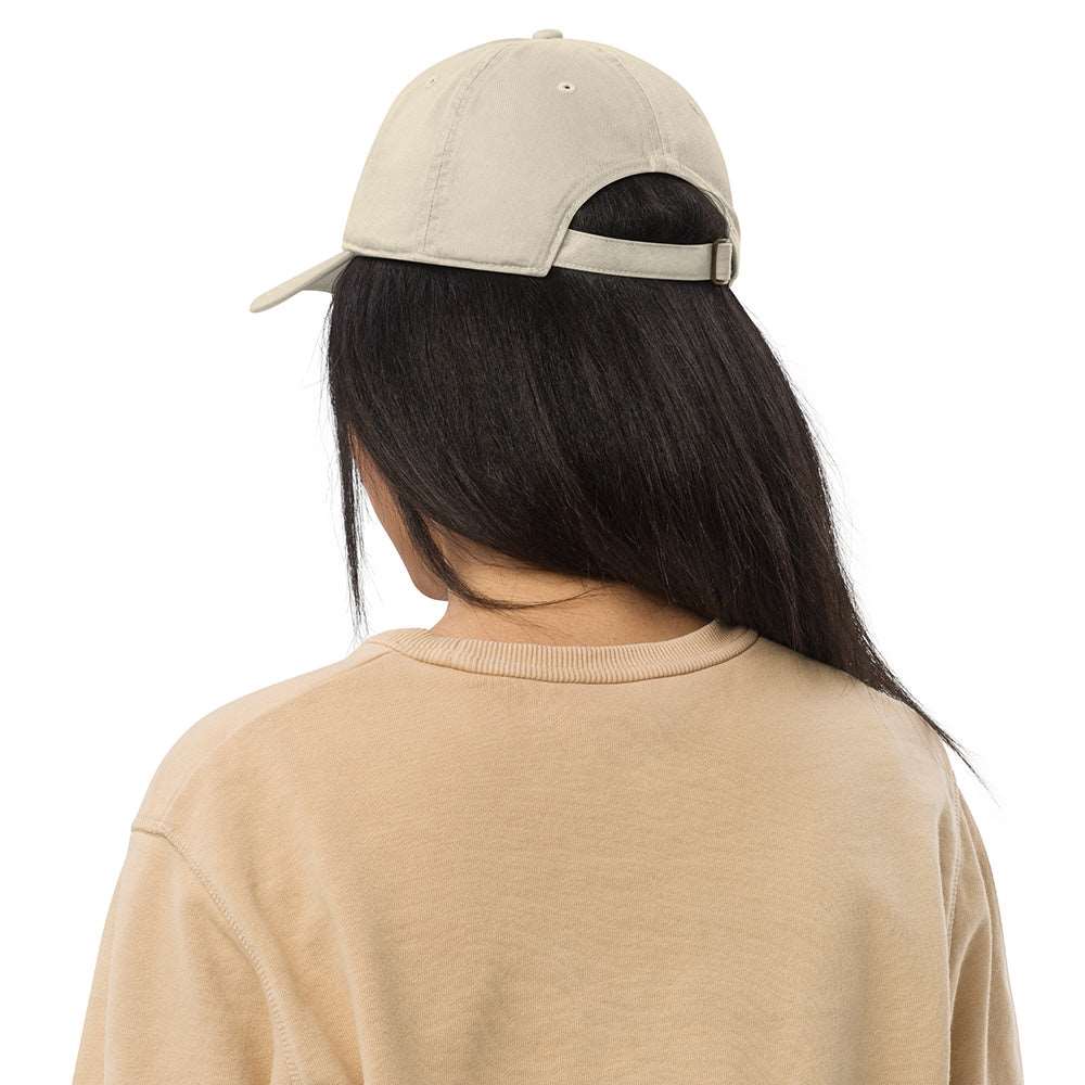 The back of a woman wearing a light tan baseball cap made of 100% organic cotton. It shows an adjustable band.