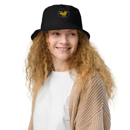 Duck Organic Bucket Hat. A woman wearing a black bucket hat made of 100% organic cotton with a large yellow duck with purple details embroidered on the front.