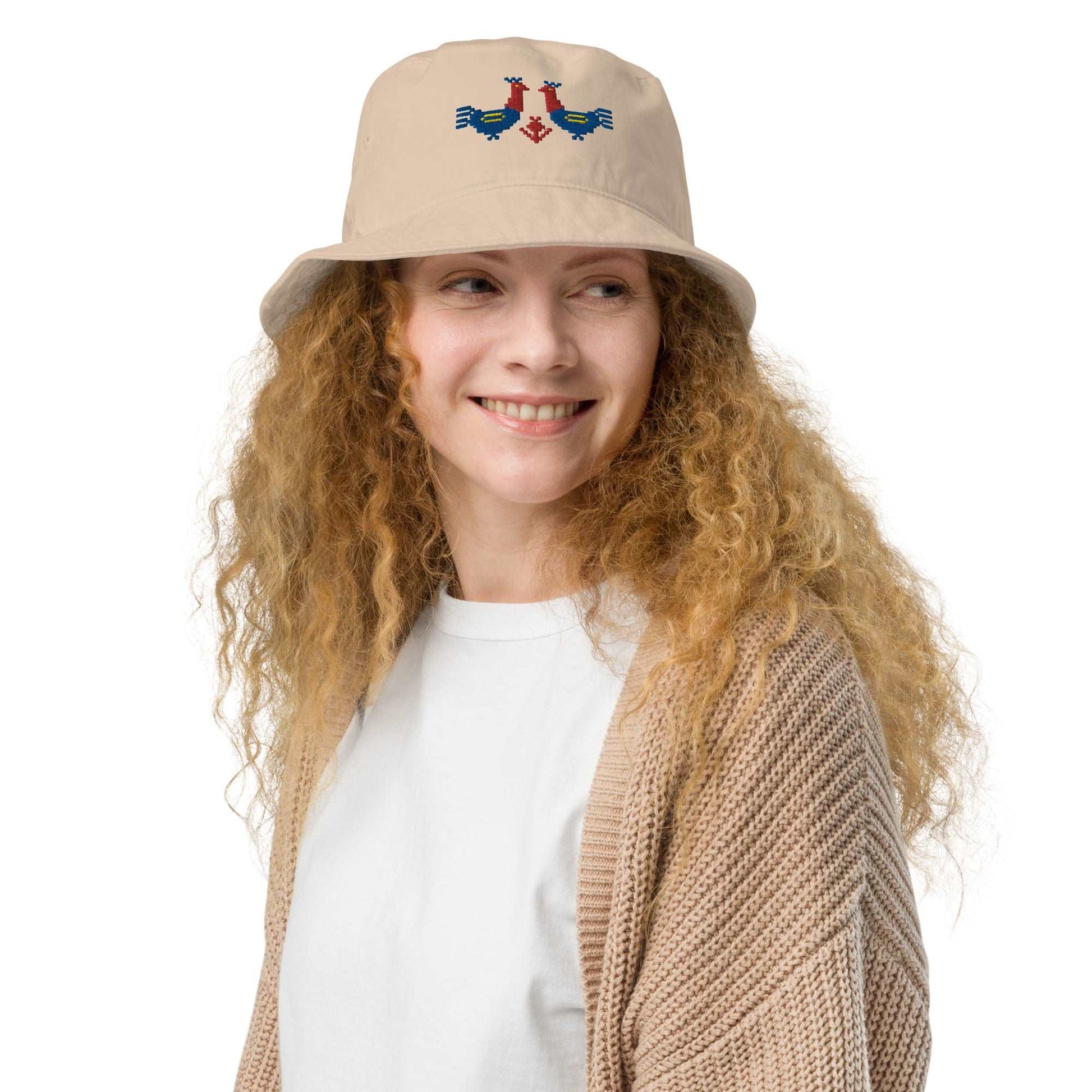 Roosters Organic bucket hat, Roosters Organic bucket hat, a woman wearing a tan bucket hat with a pair of large red and blue roosters with yellow details embroidered on the front.