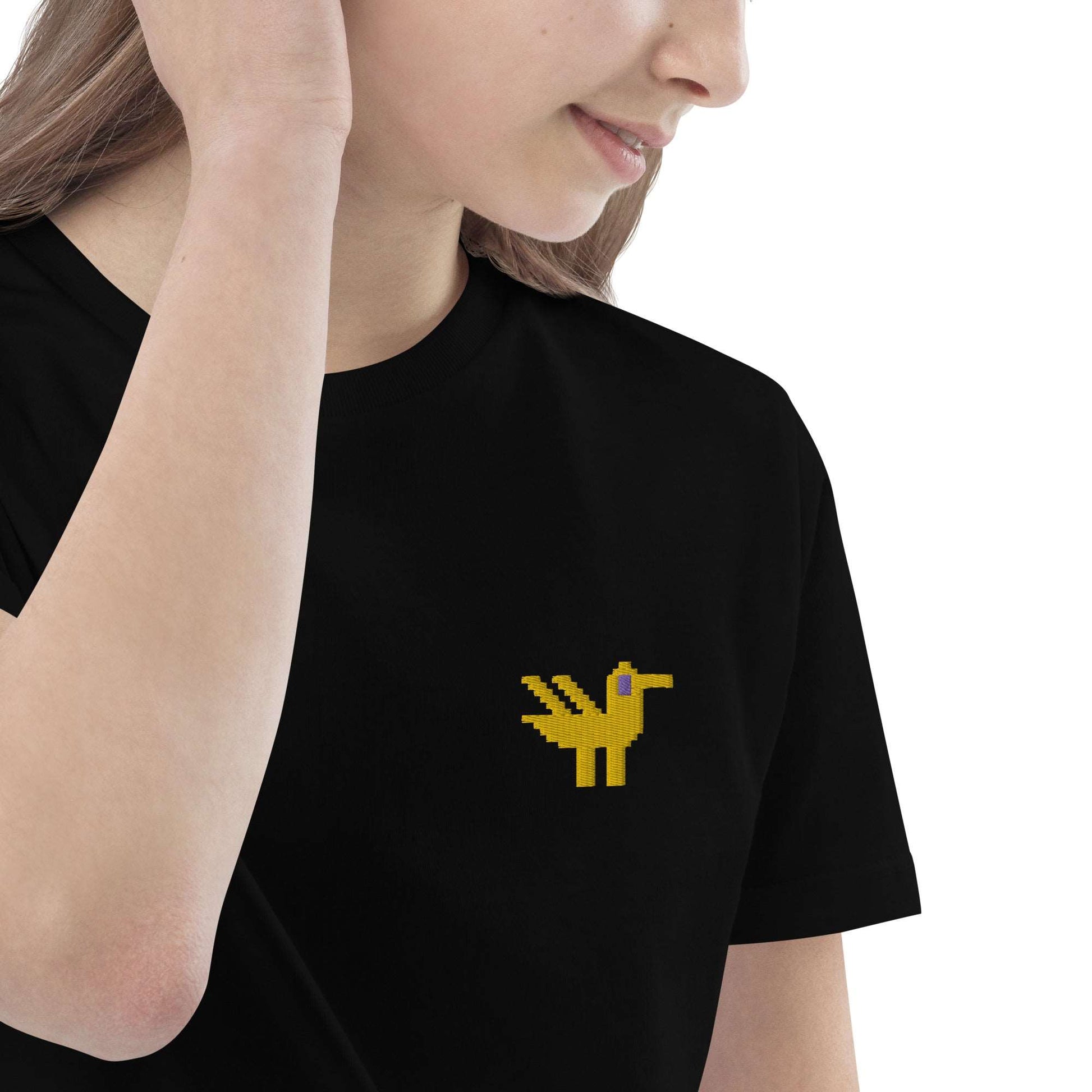 A close-up of a girl wearing a black kids t-shirt made of 100% organic cotton with a yellow duck embroidered on the top left.