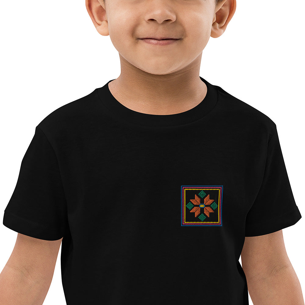 A close-up of a boy wearing a black organic cotton t-shirt with an orange flower design embroidered on the top left. The flower is enclosed within three borders of yellow, pink, and blue.