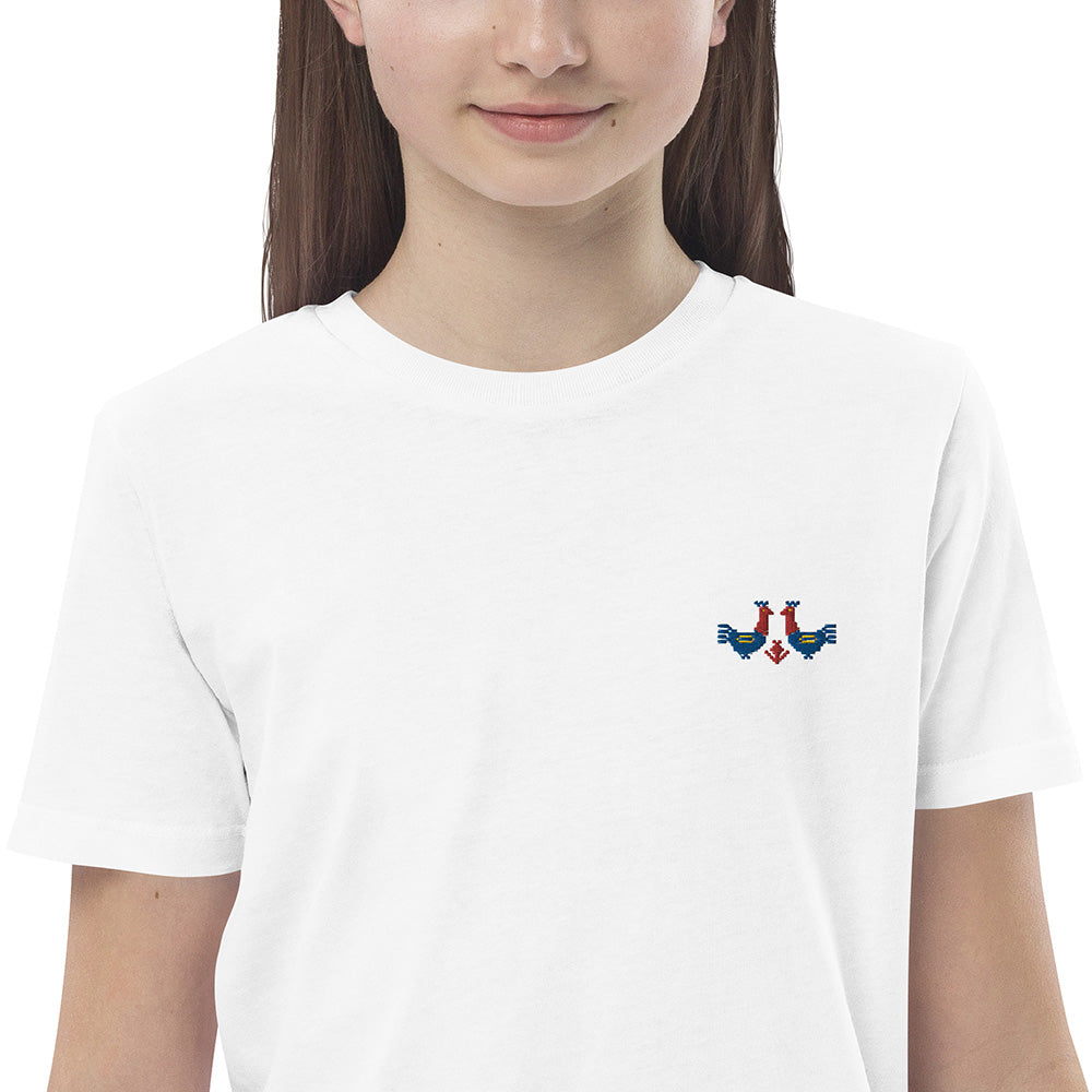 A close-up of a girl wearing a white t-shirt made of 100% organic cotton with a pair of red and blue roosters embroidered on the top left.