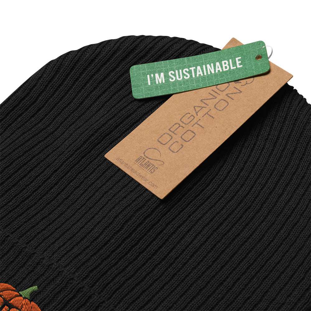 Detail of the tags on a black beanie with a pumpkin embroidered on the front. The pumpkin is wearing glasses. The tags say "I'm sustainable" and "organic cotton".