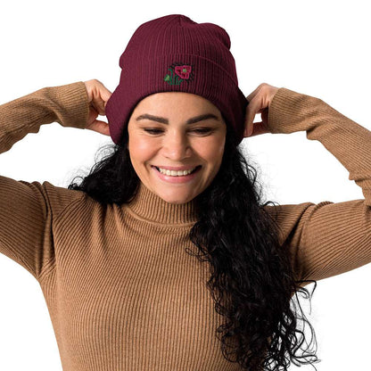 A woman wearing a burgundy ribbed beanie made of 100% organic cotton with an intricate pink flower embroidered on the front.