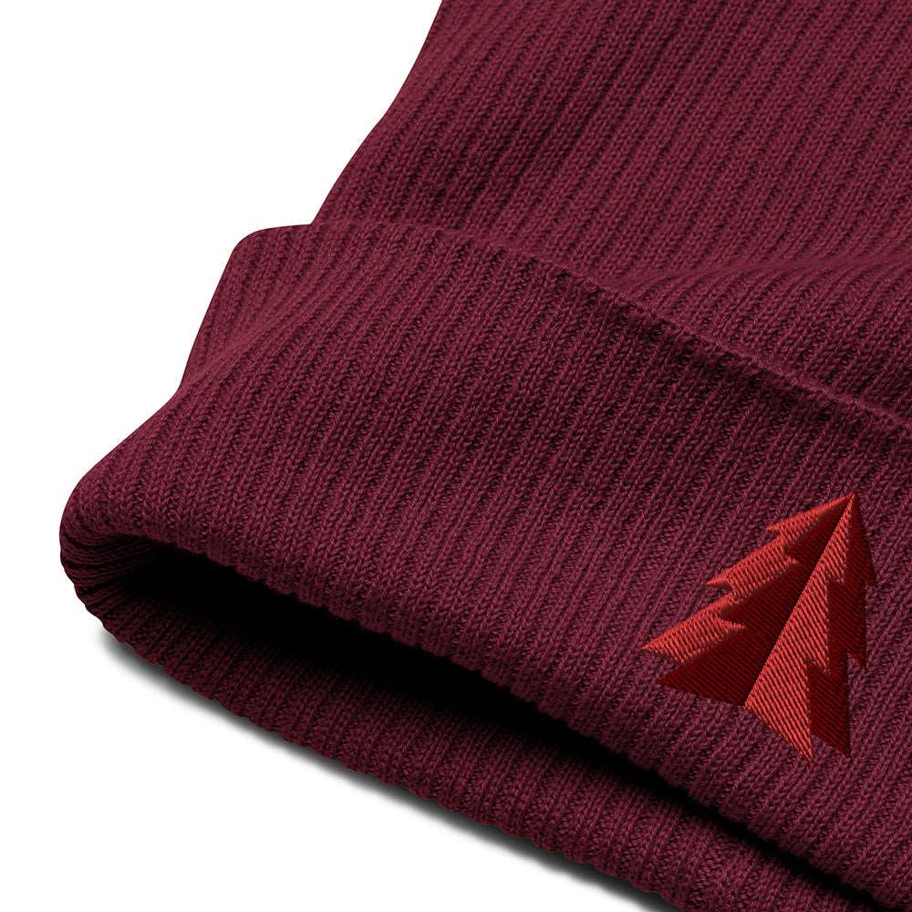 A close-up of the embroidery and cuff on a festive holiday burgundy ribbed beanie made of 100% organic cotton with an embroidered minimalist two-tone tree on the front.