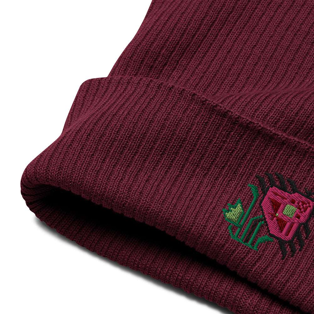 A close-up of the cuff and embroidery on a burgundy ribbed beanie made of 100% organic cotton with an intricate pink flower embroidered on the front.