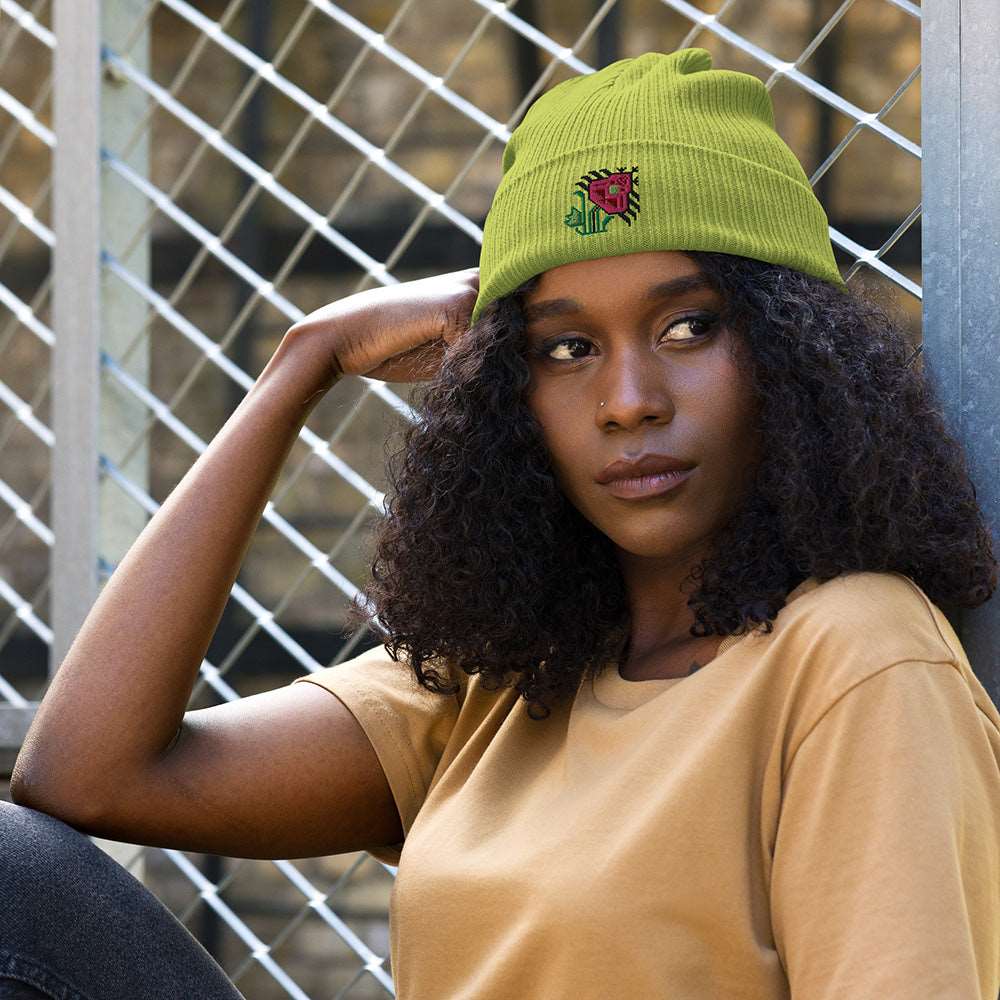 A woman wearing a light green ribbed beanie made of 100% organic cotton with an intricate pink flower embroidered on the front.