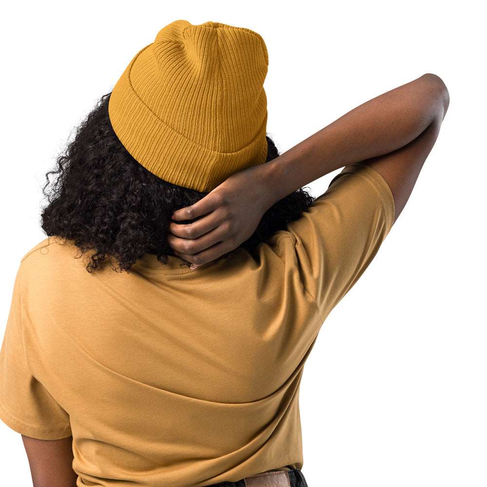 The back of a woman wearing a mustard yellow ribbed beanie made of 100% organic cotton.