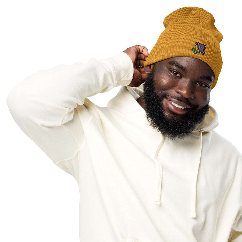 A man wearing a mustard yellow ribbed beanie made of 100% organic cotton with an intricate purple flower embroidered on the front.