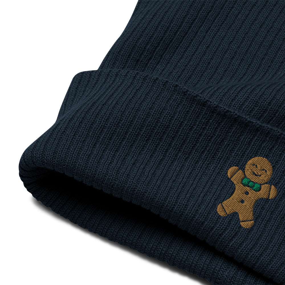 A close-up of the embroidery on the cuff of a navy blue ribbed festive holiday beanie with a gingerbread man embroidered on the front. The beanie is made of 100% organic cotton.