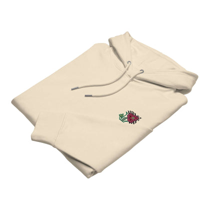 A light tan hoodie made of organic cotton and recycled polyester with an intricate pink flower embroidered on the top left. It is folded to show the embroidery detail.