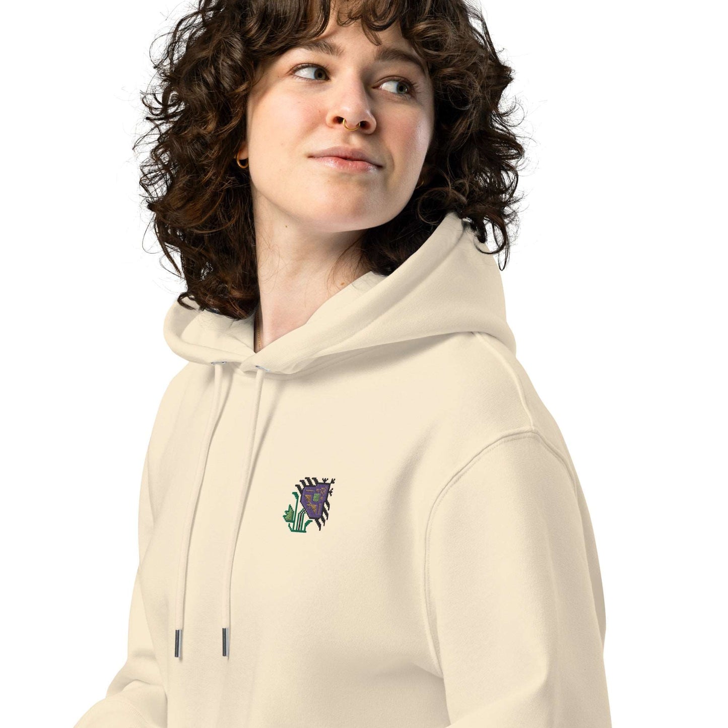 A close-up of a woman wearing a light tan hoodie made of organic cotton and recycled polyester with an intricate purple flower embroidered on the top left.