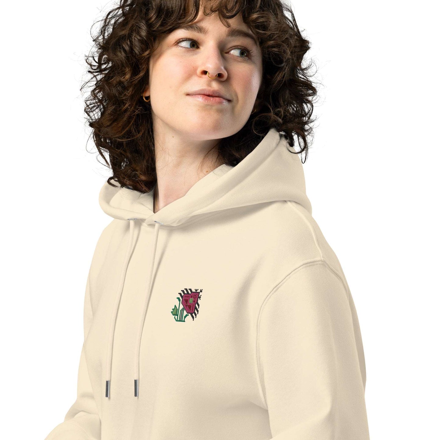 A close-up of a woman wearing a light tan hoodie made of organic cotton and recycled polyester with an intricate pink flower embroidered on the top left.