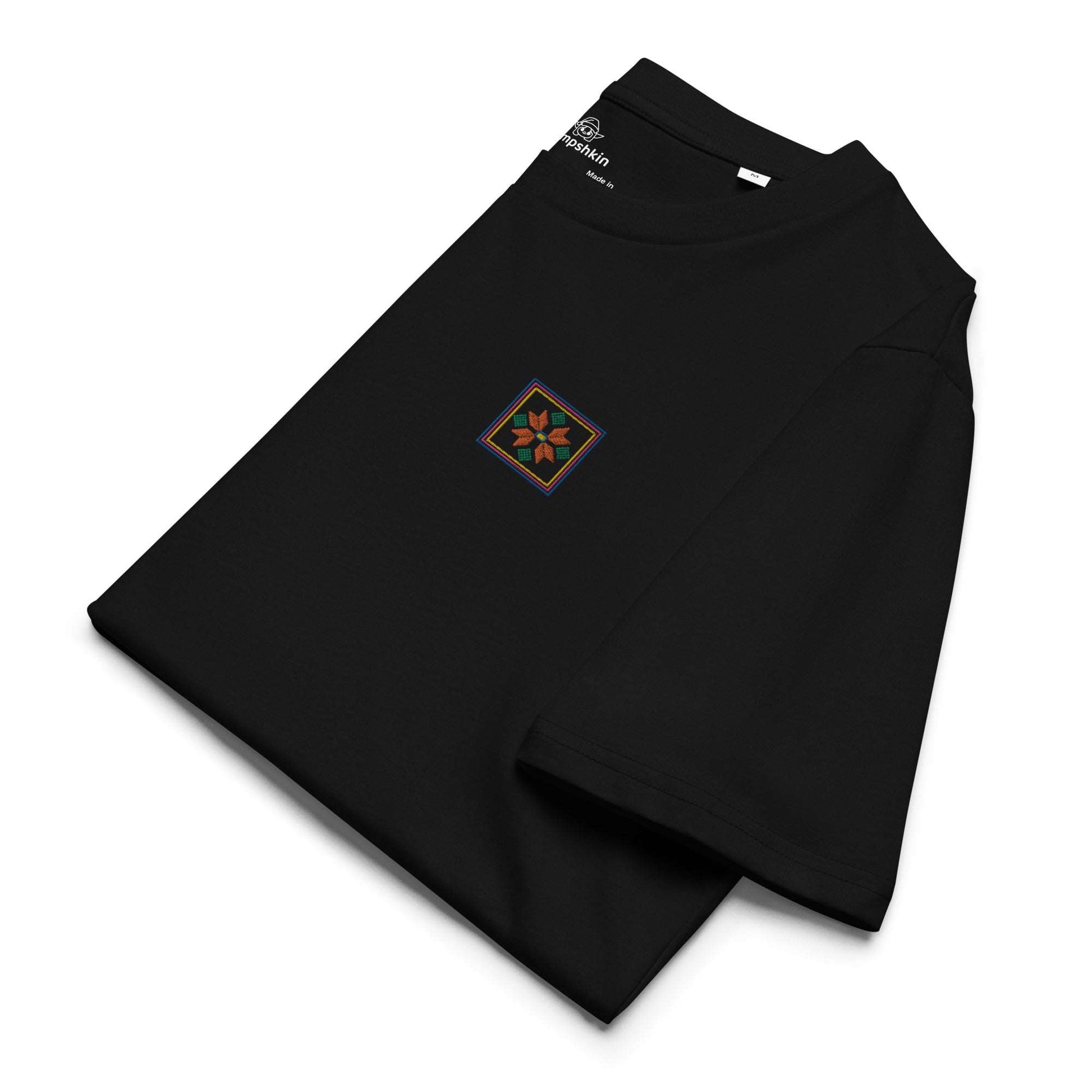 A black organic cotton t-shirt with an orange flower design embroidered on the top left. The flower is enclosed within three borders of yellow, pink, and blue. The t-shirt is folded to show the top left embroidered detail and the left sleeve.