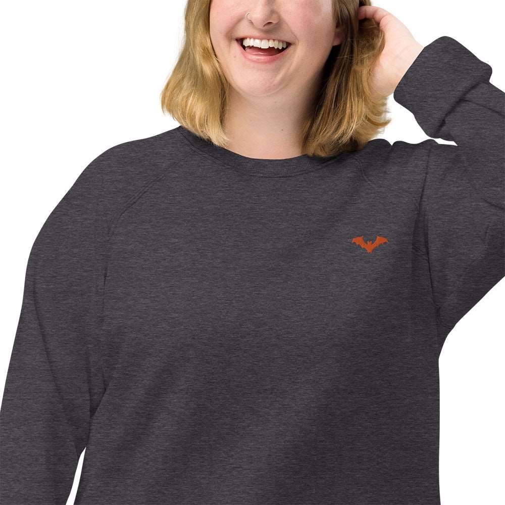 Closeup of a woman wearing a spooky Halloween charcoal grey sweatshirt with a small orange bat embroidered on the top left.