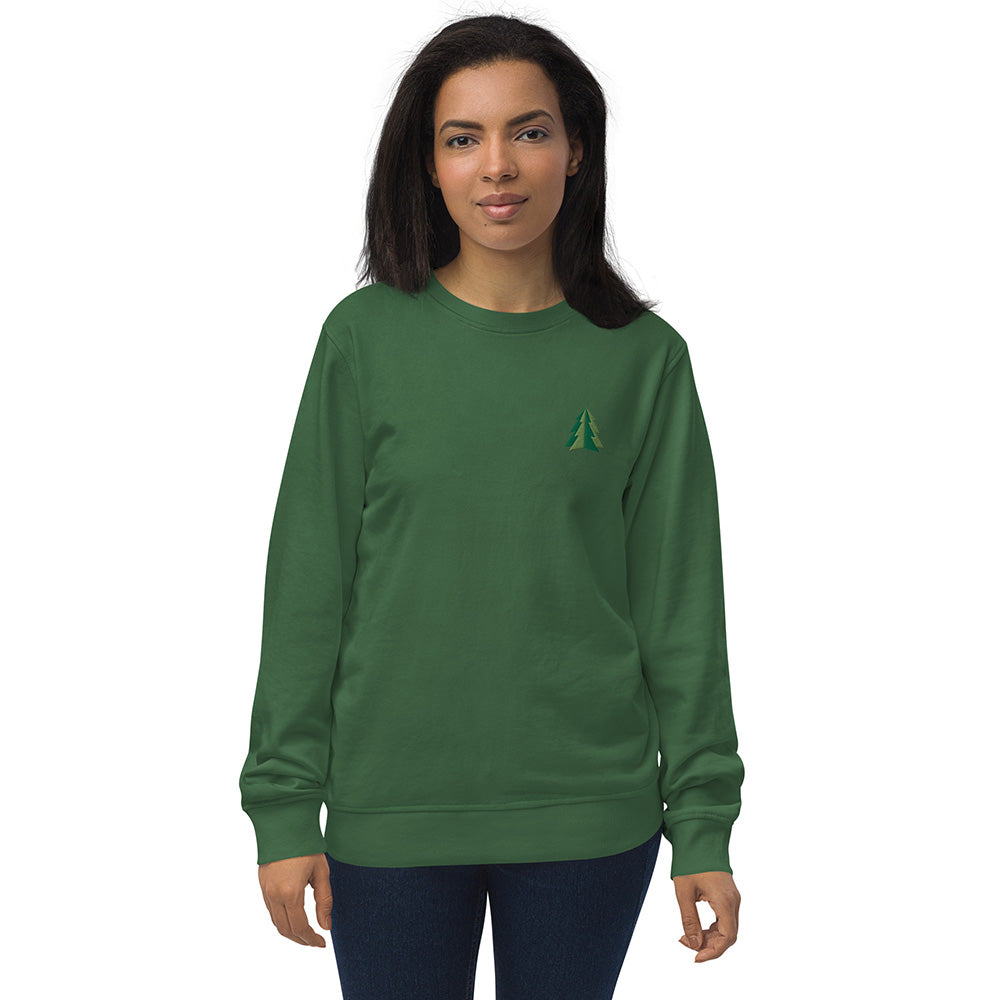 A woman wearing a festive green Christmas sweatshirt made of organic cotton and recycled polyester with a small minimalist two-tone pine tree embroidered on the top left.