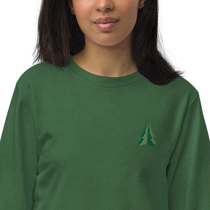 A closeup of a woman wearing a festive green Christmas sweatshirt made of organic cotton and recycled polyester with a small minimalist two-tone pine tree embroidered on the top left.